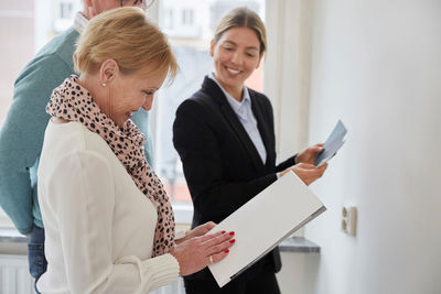 Smiling agent looking at senior couple with brochure deciding color samples for new house