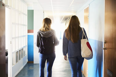 Rear view of friends walking in corridor at university on sunny day