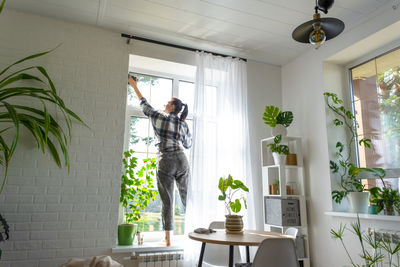 Portrait of woman standing by potted plant against wall