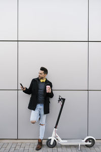 Young man using phone while standing on wall