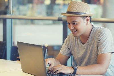 Smiling man wearing hat using laptop at cafe