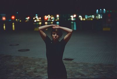 Portrait of young woman posing against illuminated street