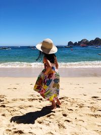 Full length of girl wearing hat standing at beach against clear sky