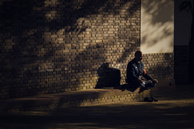 Mature man sitting against brick wall