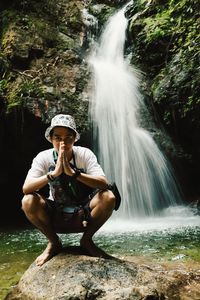 Man standing on rock against waterfall in forest