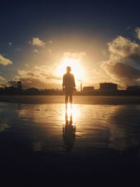 Rear view of silhouette man standing in sea against sunset sky