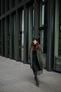 Full length portrait of woman standing against wall