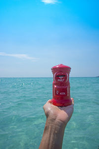 Midsection of person holding sea against blue sky