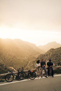 Young male and female friends talking while sitting roadside at sunset on vacation