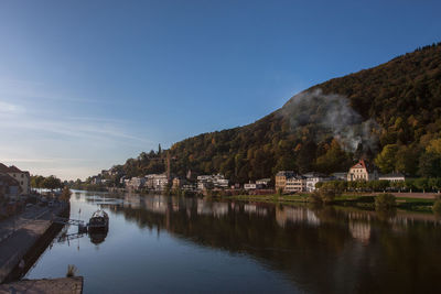 Houses on riverbank by tree mountain against sky