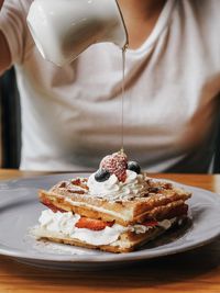 Midsection of woman pouring syrup on food in plate