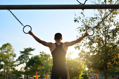 Rear view of man exercising with gymnastic rings against sky