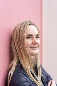 Young smiling woman looking at camera in front of wall outdoors