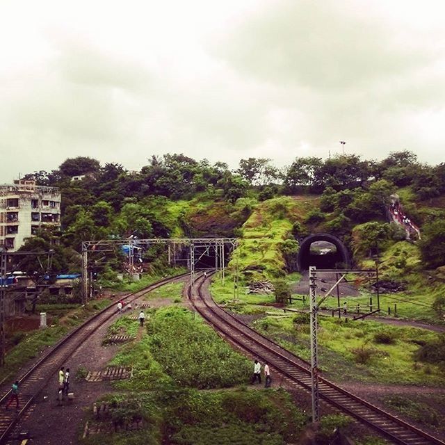 transportation, sky, tree, land vehicle, railroad track, road, mode of transport, car, architecture, built structure, building exterior, cloud - sky, rail transportation, public transportation, street, high angle view, train - vehicle, day, cloudy, outdoors