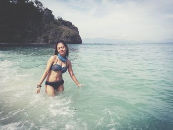 Woman wearing bikini while standing in sea against mountain