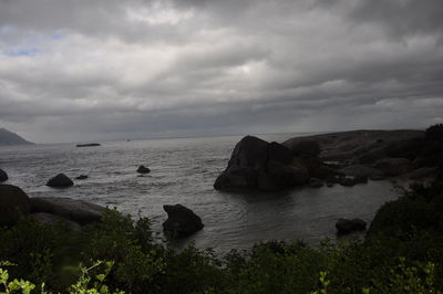 Scenic view of sea and rocks against cloudy sky