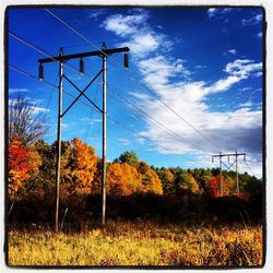 Electricity pylon on field against cloudy sky