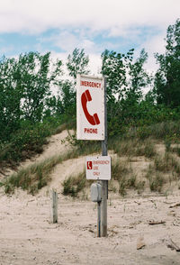 Information sign on road by trees against sky