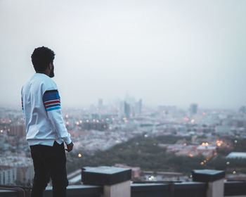 Rear view of man looking at city buildings against sky