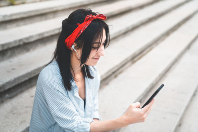 Young woman using phone while sitting on staircase