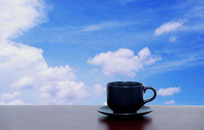 Coffee cup on table against blue sky