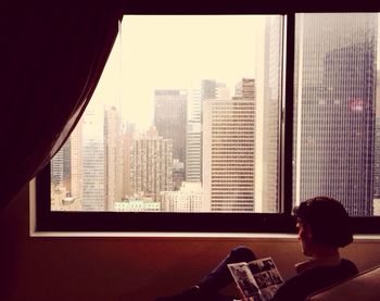 Rear view of man reading magazine by window at home
