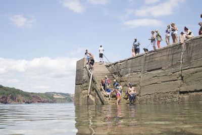 People on rock by sea against sky