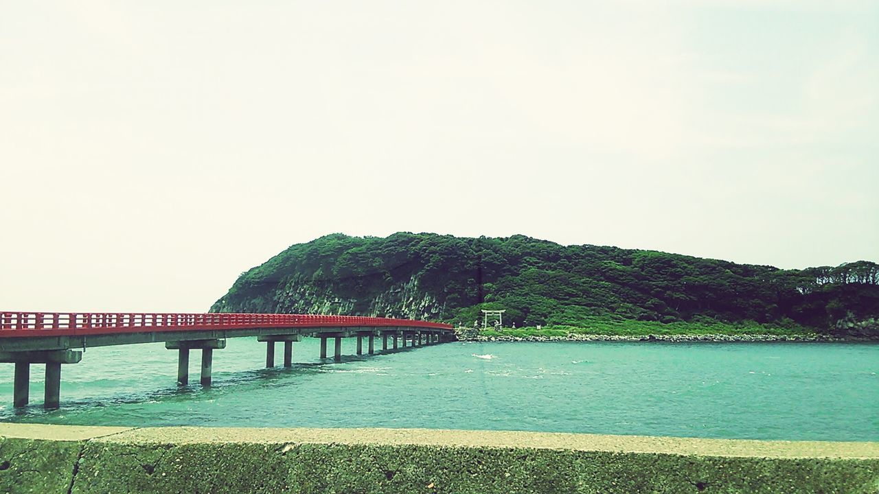 water, connection, bridge - man made structure, mountain, tree, bridge, river, tranquility, tranquil scene, railing, scenics, built structure, clear sky, beauty in nature, sky, nature, architecture, sea, copy space, transportation