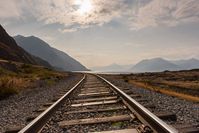 Railroad track leading towards mountains against sky