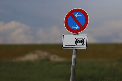 Road sign on field against sky