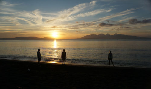 Silhouette people on beach against sky during sunset