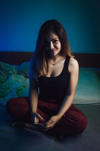 Portrait of smiling young woman sitting on bed at home