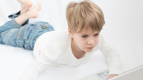 Cute boy looking away while relaxing on bed at home