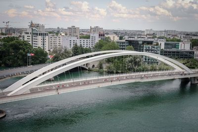 Bridge over road by buildings in city against sky