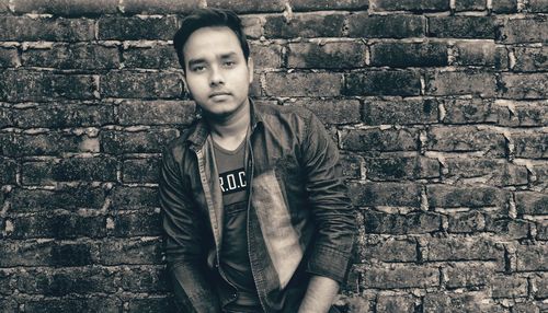 Portrait of young man standing against brick wall