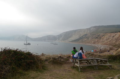 Rear view of couple sitting on bench against sky