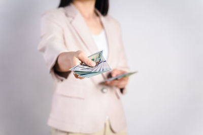 Midsection of woman holding paper while standing against white background