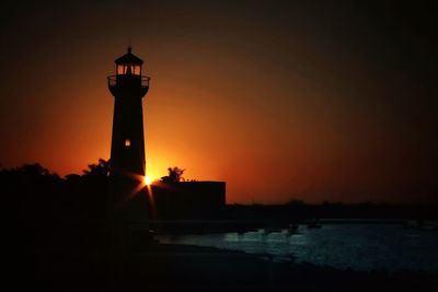 Lighthouse by sea against sky during sunset