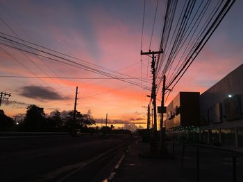 Silhouette road by electricity pylons against sky during sunset