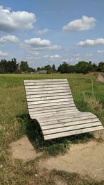 Empty bench on field against sky