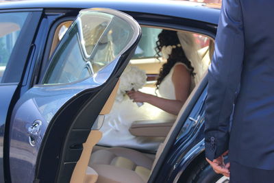 Midsection of man standing against bride sitting in car