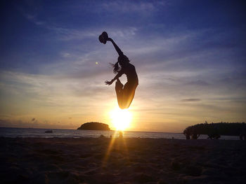 Silhouette woman jumping at beach against sky during sunset