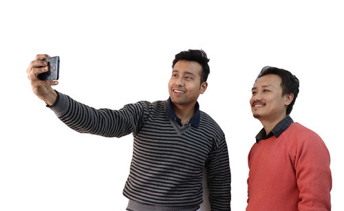 Young man photographing with mobile phone against white background