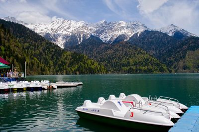 Boats moored on lake by snowcapped mountains against sky