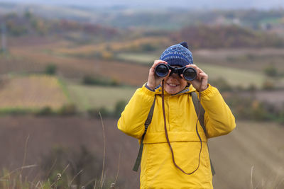 Happy little boy looking through binoculars during autumn day on a hill. copy space.