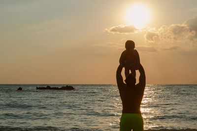 Silhouette father and son in sea against sky during sunset
