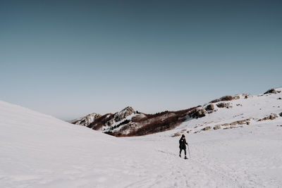 Rear view of man walking on snowcapped mountain against sky