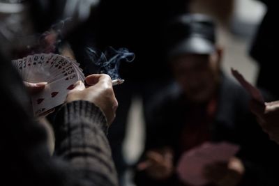 Cropped hands holding cigarette while playing cards