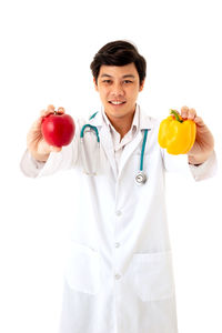 Doctor holding apple and bell pepper against white background