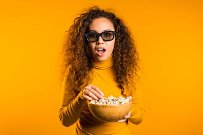 Portrait of young woman with orange against yellow background